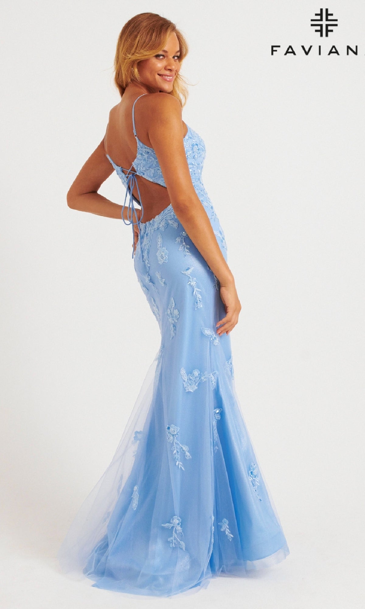 A woman models the Faviana 11229 Shimmer Tulle V-Neck Prom Dress, a light blue fit-and-flare gown with floral lace appliqué, embroidery, a lace-up back, and a mermaid silhouette. The Faviana logo is displayed.